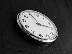 Close-up of a wall clock against a dark textured background, highlighting the time in black and white.