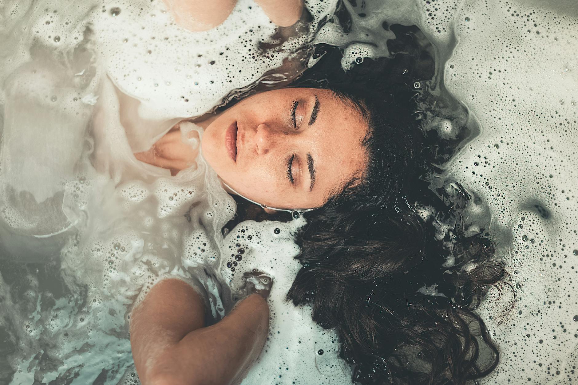 Young woman submerged in a relaxing bubble bath, eyes closed in tranquility.