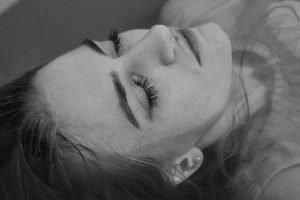 Black and white of relaxed lady with closed eyes lying in bathroom with hair immersed in water at home inside
