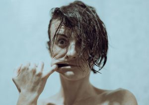 Close-up of a woman's face with wet hair and a unique expression, set against a blue background.