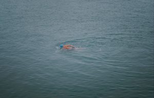 A male swimmer in a blue cap swims in open water, competing in a race.