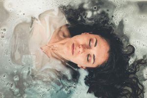 A serene woman with closed eyes floating in a soothing bubble bath, capturing a moment of peaceful relaxation.