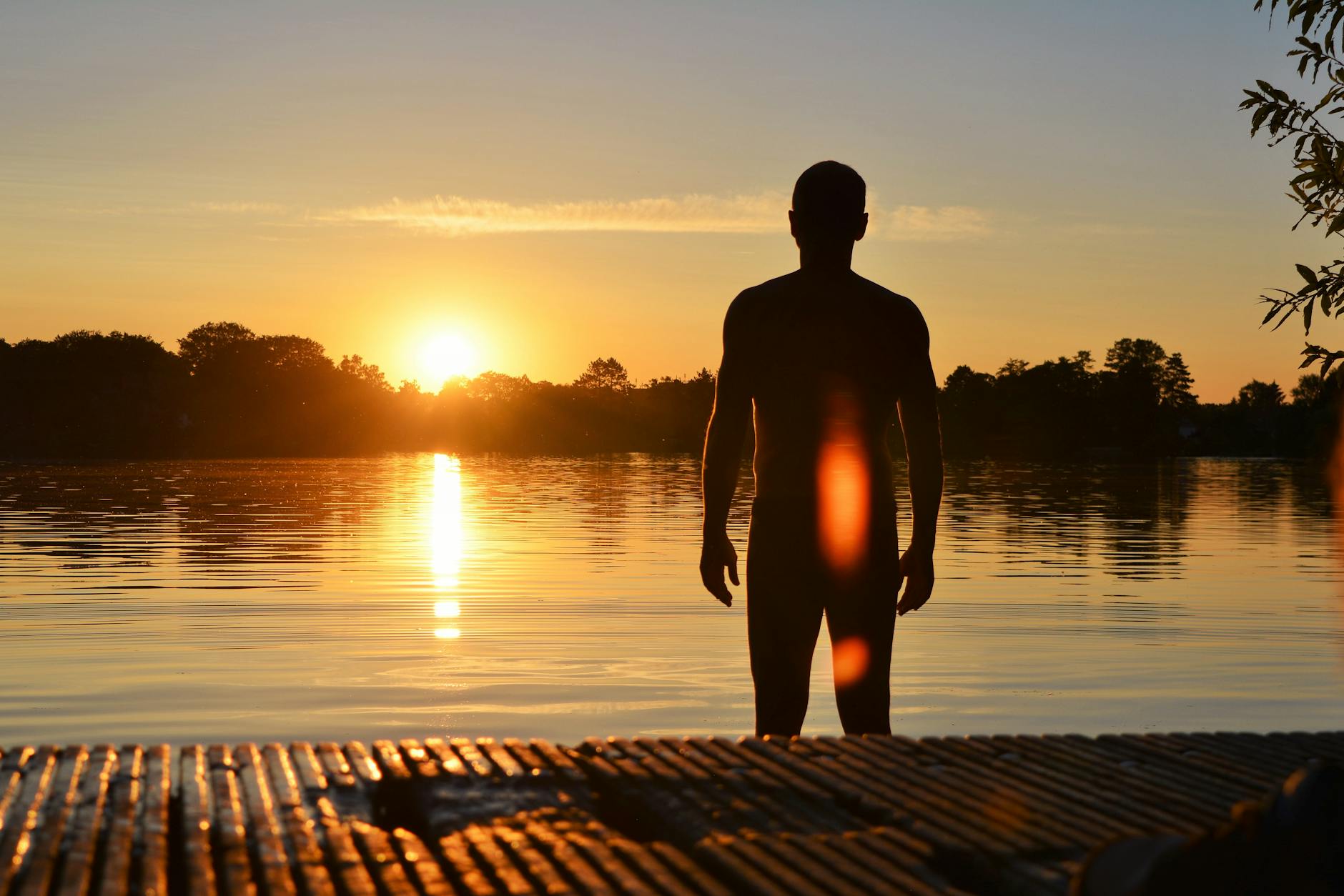 Silhouette of a man standing by a serene lake during a stunning sunset.
