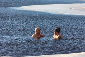 Two men enjoying winter swimming in icy waters, showcasing extreme cold exposure.