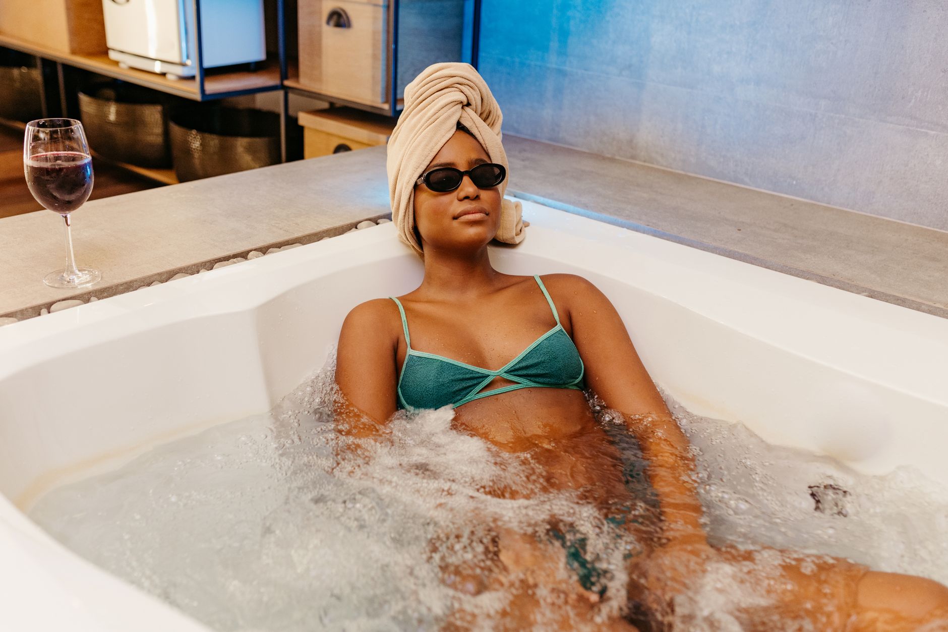 Woman enjoying a jacuzzi bath with a towel wrap and wine, exuding luxury and relaxation.